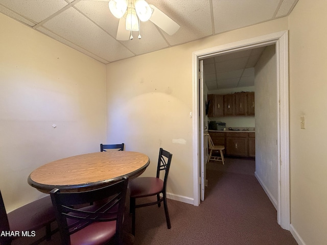 carpeted dining space with ceiling fan and a drop ceiling