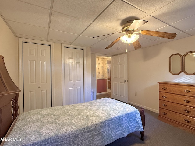 carpeted bedroom with a paneled ceiling, ceiling fan, and multiple closets