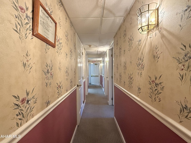 corridor with dark colored carpet and a paneled ceiling