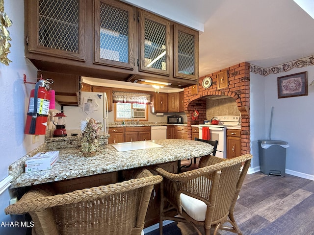 kitchen with light stone countertops, dark hardwood / wood-style floors, kitchen peninsula, white appliances, and a breakfast bar area