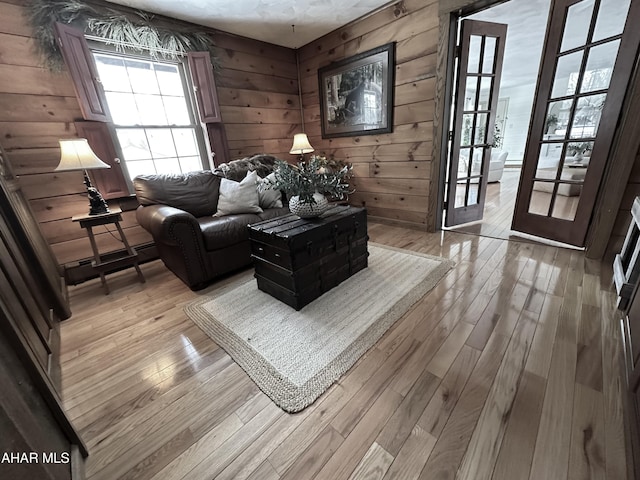 living room with baseboard heating, french doors, wooden walls, and light hardwood / wood-style flooring