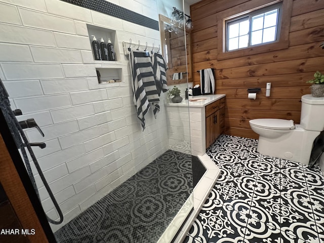 bathroom featuring wooden walls, toilet, tile patterned flooring, and a tile shower