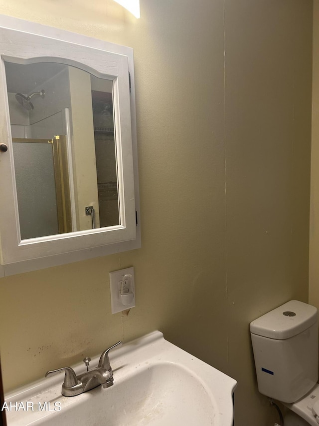 bathroom featuring sink, a shower with shower door, and toilet