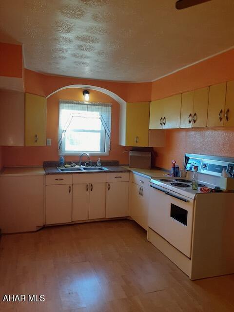 kitchen with a textured ceiling, sink, light hardwood / wood-style floors, and white stove