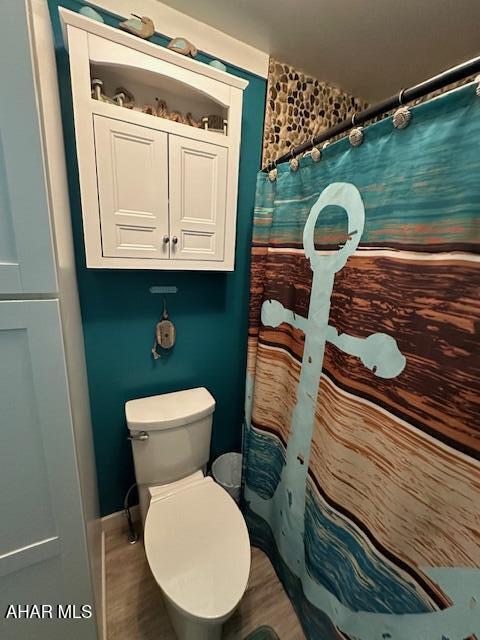 bathroom featuring wood-type flooring, toilet, and a shower with curtain