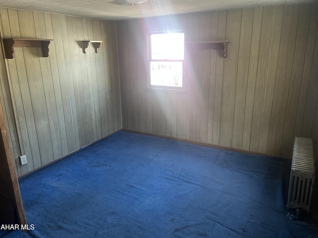 empty room featuring carpet flooring, wooden walls, and radiator