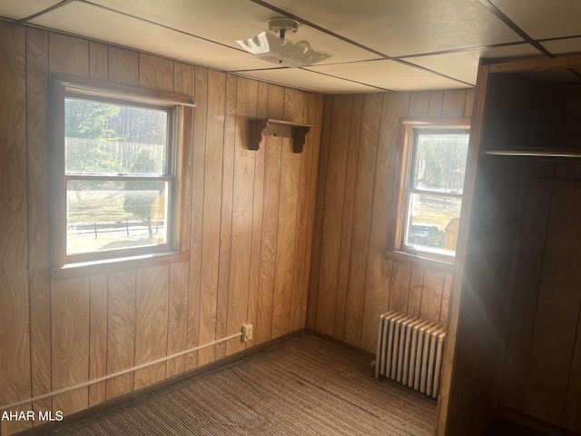 empty room featuring wooden walls, radiator heating unit, and carpet