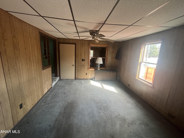 interior space with wooden walls, a ceiling fan, and a drop ceiling