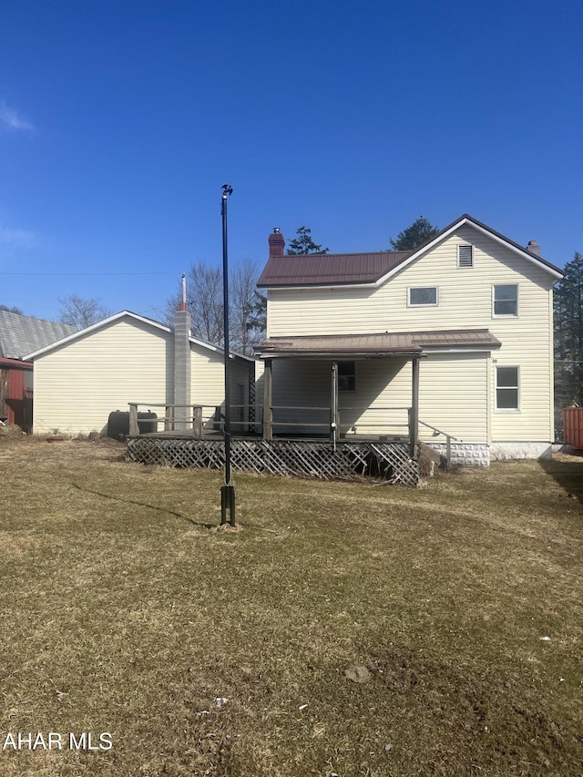 back of house featuring a chimney, metal roof, and a yard