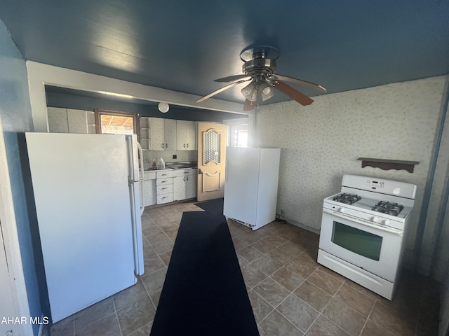 kitchen with a wealth of natural light, a ceiling fan, white appliances, white cabinets, and wallpapered walls