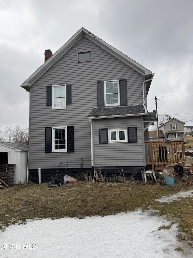 rear view of property featuring an outbuilding, a chimney, a wooden deck, and a storage unit