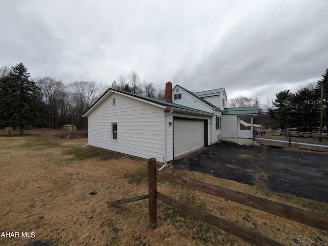 view of property exterior with a garage, a yard, a chimney, and driveway