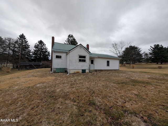 back of property featuring a chimney, metal roof, and a yard