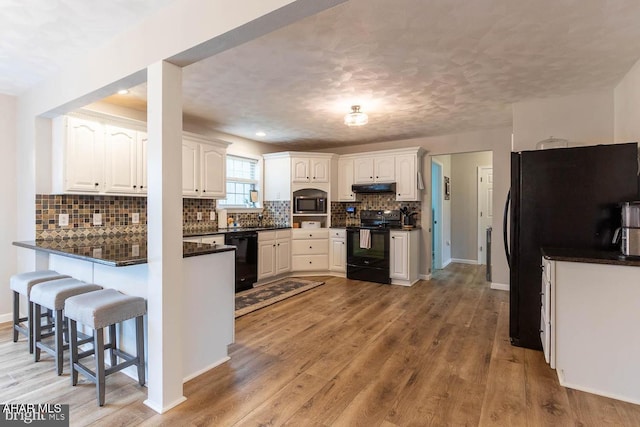 215 Oakwood Dr, Philipsburg, PA 16866 - kitchen with dark countertops, a peninsula, white cabinetry, under cabinet range hood, and black appliances