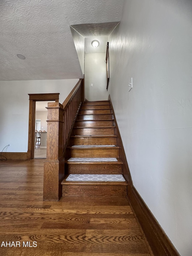 stairway with a textured ceiling, baseboards, and wood finished floors