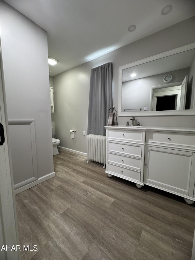 bathroom with vanity, radiator, wood finished floors, baseboards, and toilet