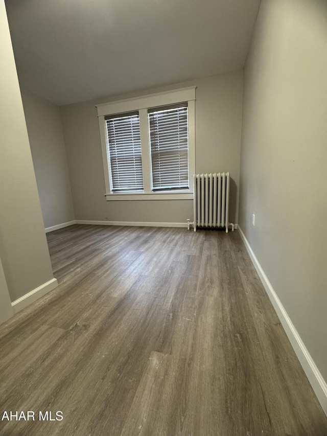 empty room with radiator, baseboards, and wood finished floors