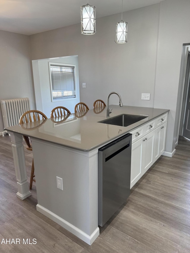 kitchen with pendant lighting, a sink, wood finished floors, white cabinets, and dishwashing machine