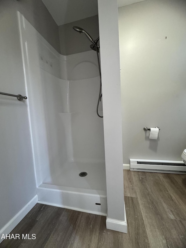 bathroom featuring wood finished floors, baseboards, baseboard heating, and a shower