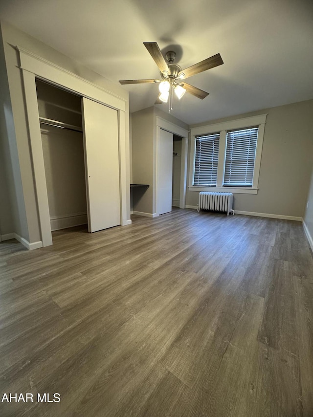 unfurnished bedroom featuring two closets, a ceiling fan, wood finished floors, radiator, and baseboards