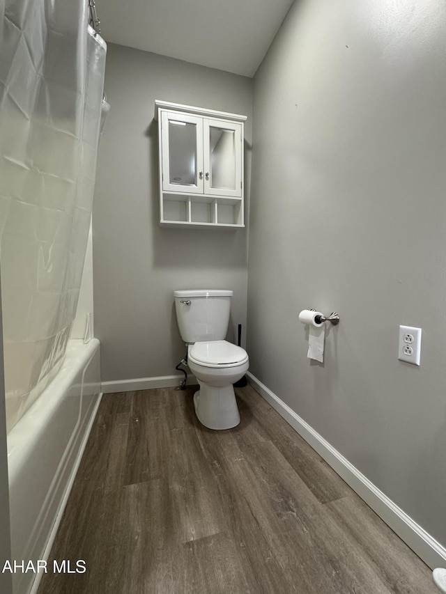 bathroom featuring toilet, shower / bath combo, baseboards, and wood finished floors