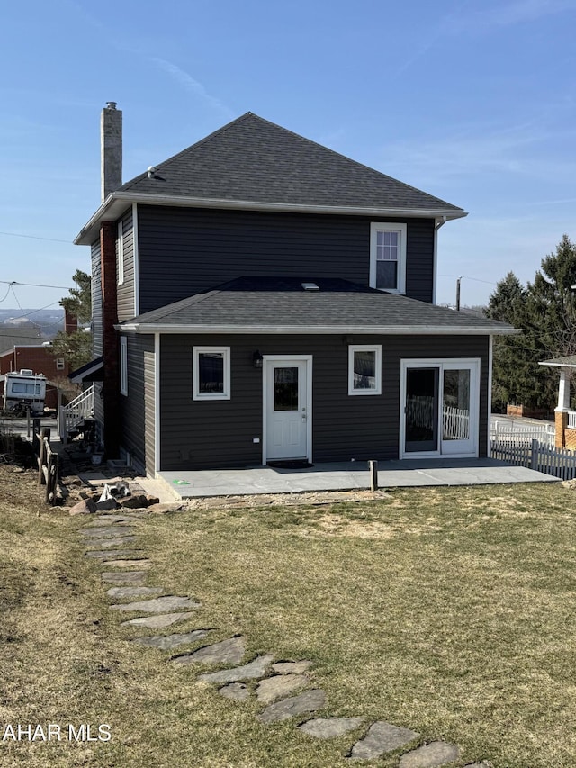 rear view of property with fence, a chimney, a shingled roof, a patio area, and a lawn