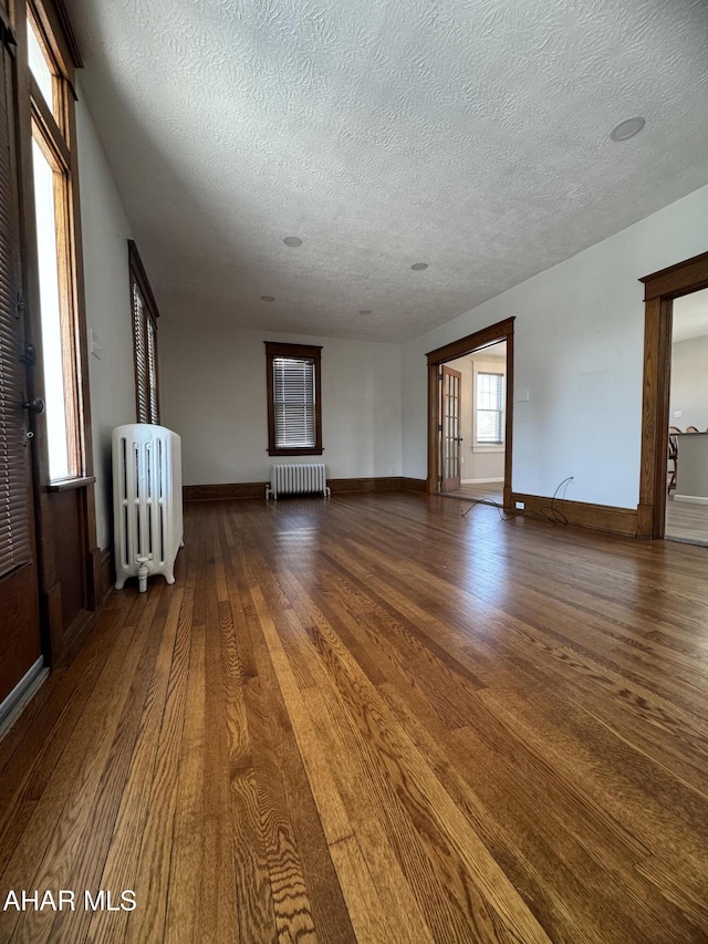 unfurnished living room with baseboards, radiator, wood finished floors, and a textured ceiling