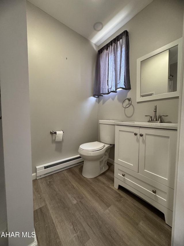 half bath with toilet, a baseboard heating unit, wood finished floors, baseboards, and vanity