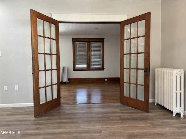 empty room with french doors, wood finished floors, and radiator heating unit