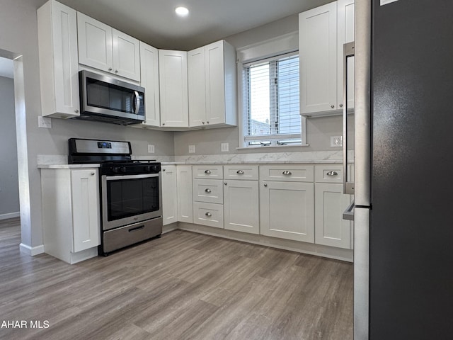 kitchen with light stone countertops, baseboards, light wood-style flooring, appliances with stainless steel finishes, and white cabinetry