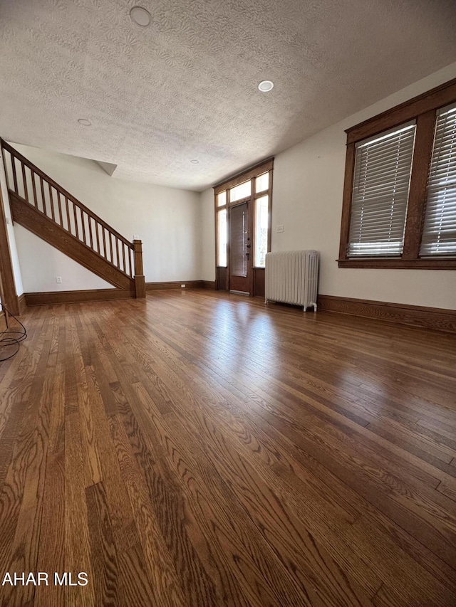 unfurnished living room featuring stairway, baseboards, radiator, and wood finished floors