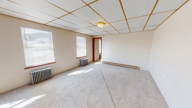 carpeted spare room featuring radiator heating unit, a baseboard heating unit, and a drop ceiling