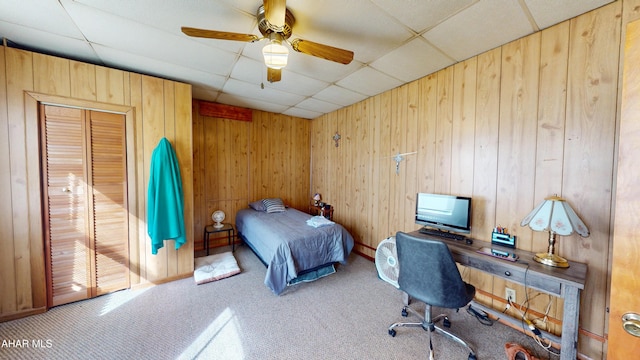 carpeted bedroom featuring a drop ceiling, wood walls, and ceiling fan