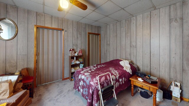 carpeted bedroom with a ceiling fan, a paneled ceiling, and wooden walls