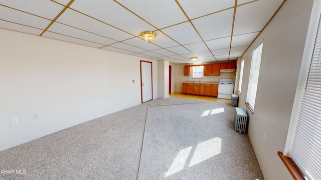 unfurnished living room featuring a paneled ceiling, light colored carpet, and radiator heating unit