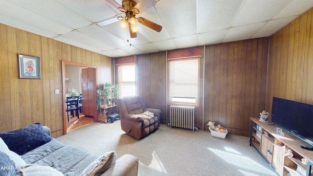 living room with light carpet, radiator heating unit, wooden walls, and ceiling fan