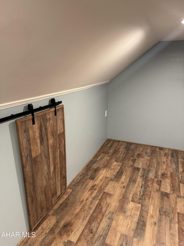 additional living space featuring wood-type flooring, a barn door, and vaulted ceiling