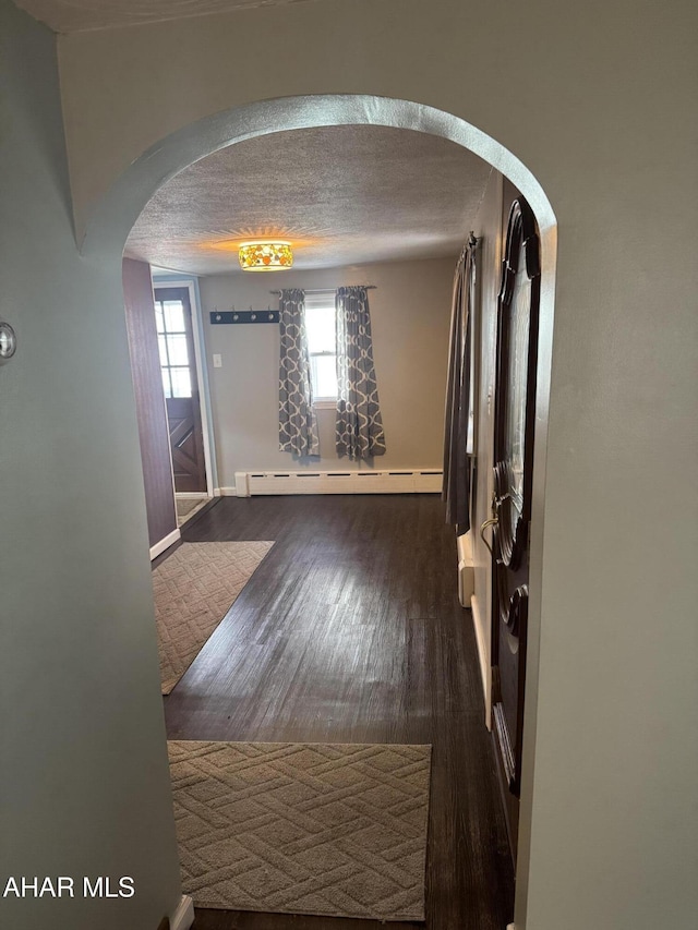 corridor with a baseboard radiator, dark wood-type flooring, and a textured ceiling