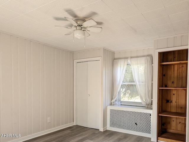 unfurnished bedroom featuring radiator, ceiling fan, wooden walls, dark hardwood / wood-style floors, and a closet