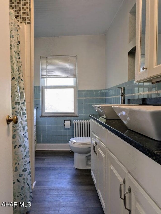 bathroom featuring vanity, radiator, hardwood / wood-style flooring, toilet, and tile walls