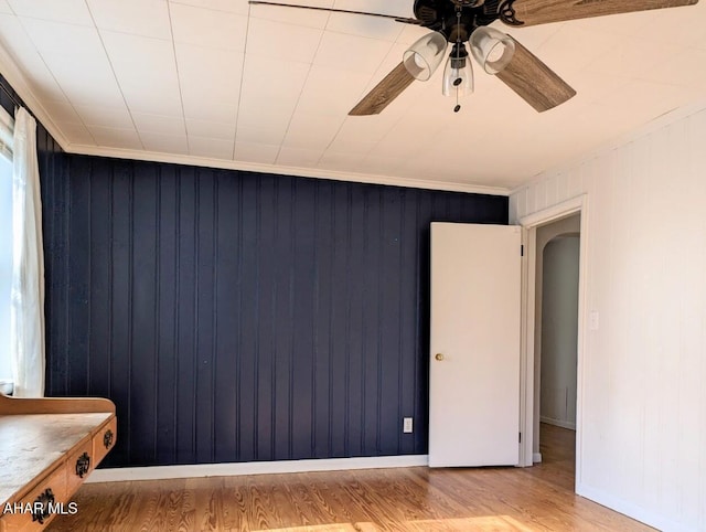 unfurnished bedroom with ceiling fan, wooden walls, and light wood-type flooring