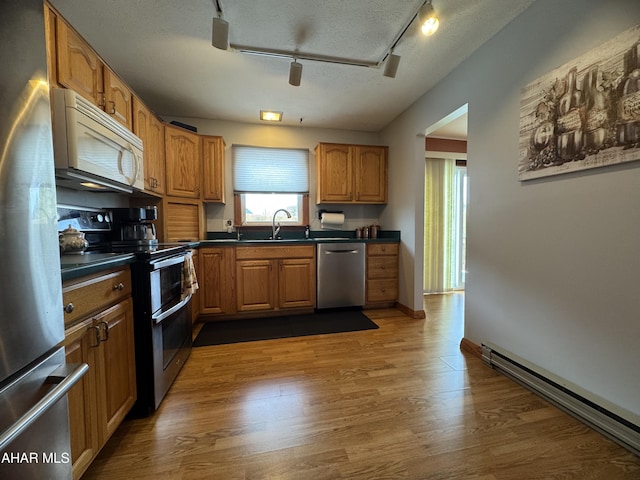 kitchen with sink, dark hardwood / wood-style flooring, baseboard heating, stainless steel appliances, and a textured ceiling