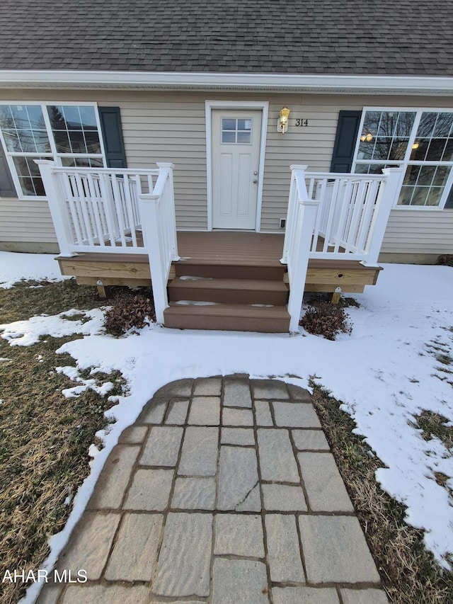 snow covered property entrance featuring a shingled roof