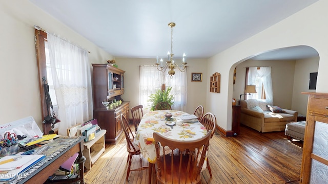 dining room featuring an inviting chandelier, a wealth of natural light, arched walkways, and light wood finished floors