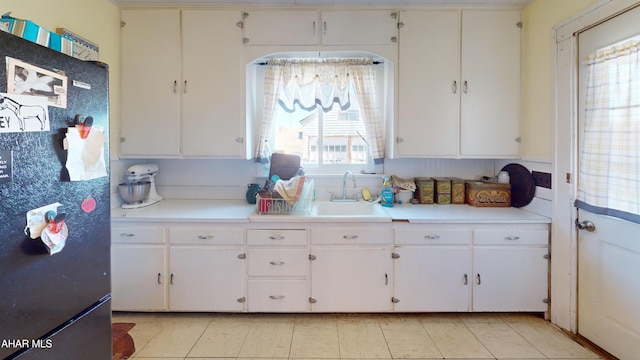 kitchen with white cabinetry, light countertops, freestanding refrigerator, and a sink