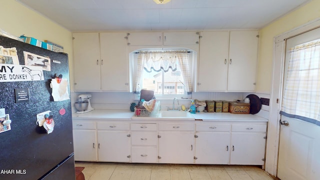 kitchen featuring white cabinetry, light countertops, freestanding refrigerator, and a sink