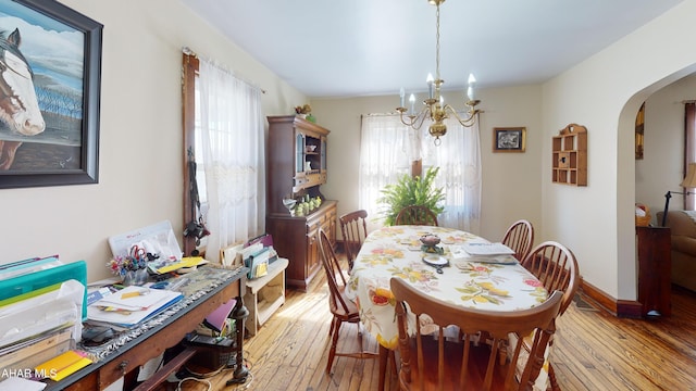 dining area with an inviting chandelier, baseboards, arched walkways, and light wood finished floors