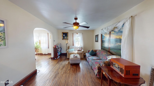 living area with arched walkways, baseboards, a ceiling fan, and wood-type flooring