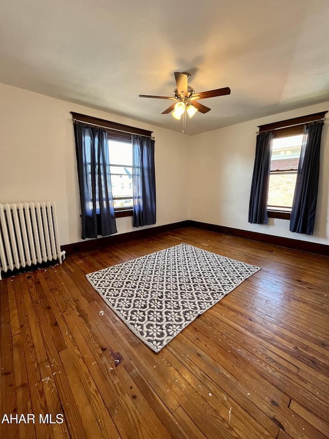 empty room with baseboards, a ceiling fan, radiator heating unit, and hardwood / wood-style flooring