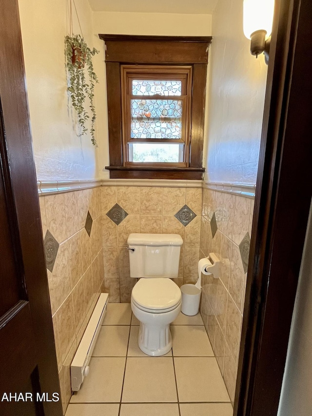 half bath with tile patterned floors, baseboard heating, wainscoting, and toilet